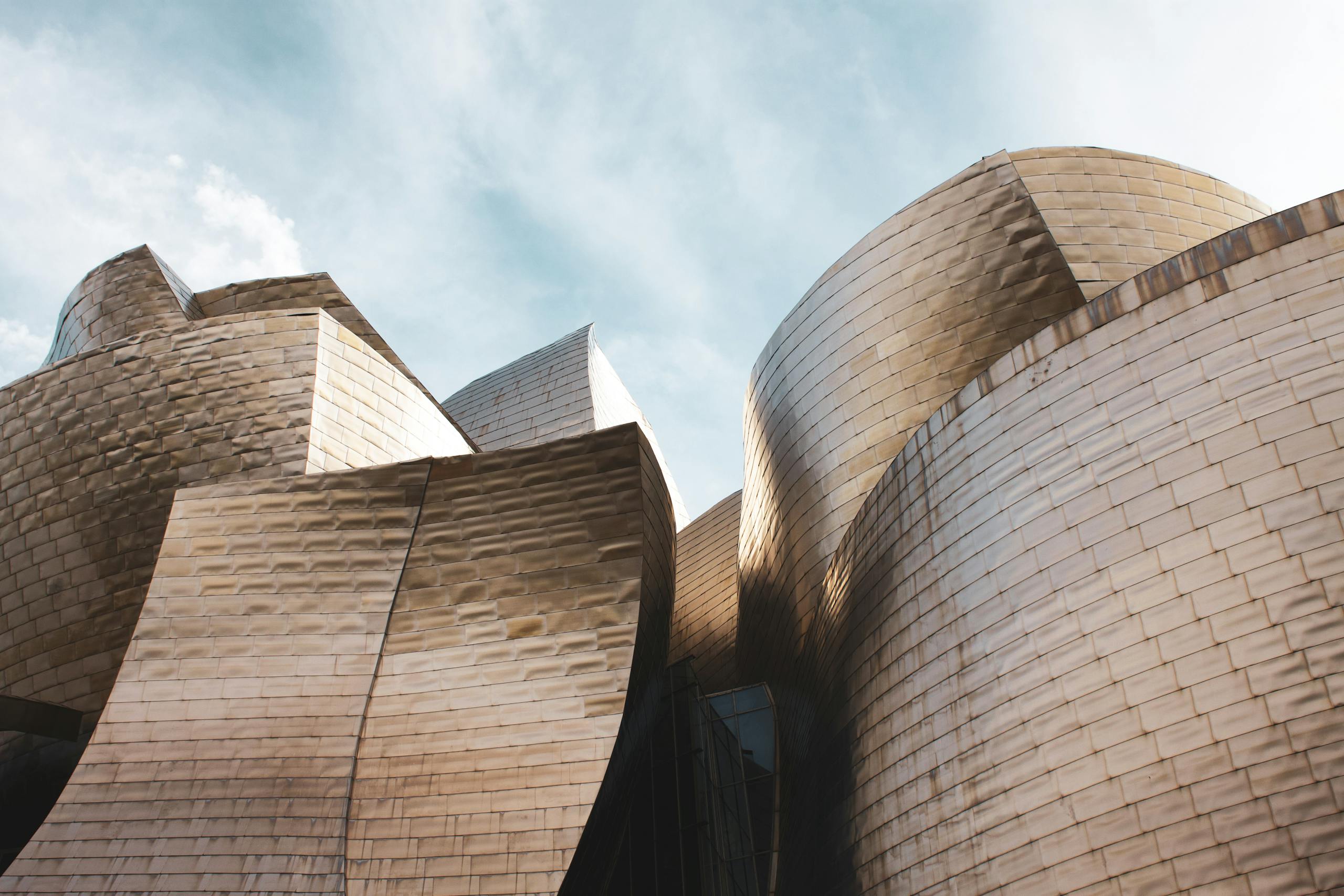 Low angle view of Guggenheim Museum Bilbao's modern architecture under a bright sky.