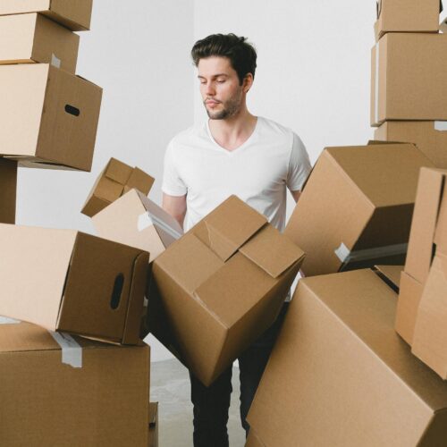 A young man surrounded by moving boxes indoors, contemplating unpacking.