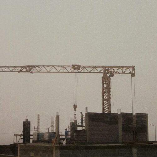 A misty, early morning view of a construction site with a crane and workers building amidst dense fog.