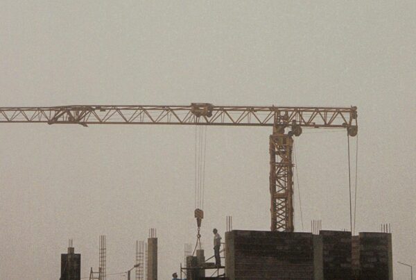 A misty, early morning view of a construction site with a crane and workers building amidst dense fog.