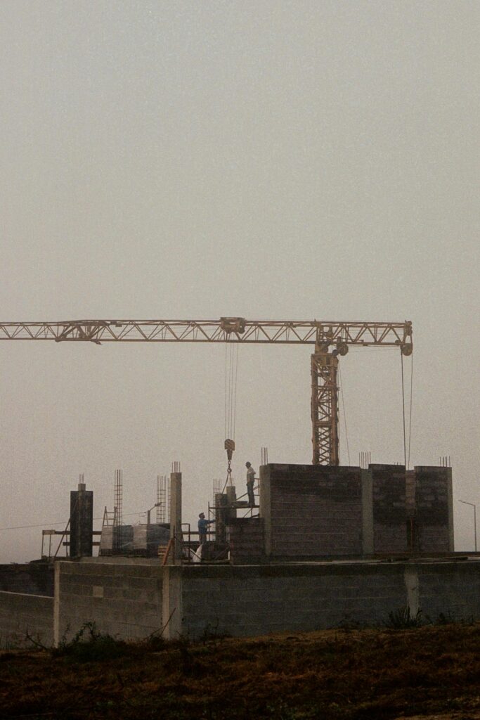 A misty, early morning view of a construction site with a crane and workers building amidst dense fog.